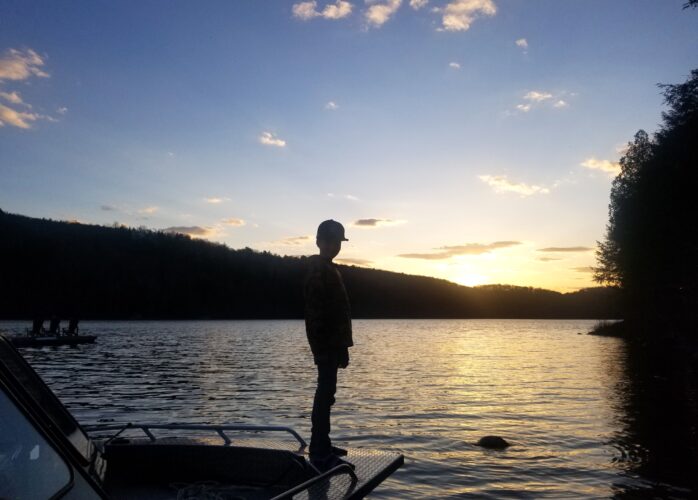 Boy standing on boat at sunset